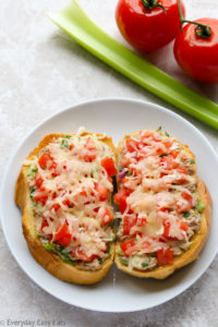 Overhead view of an Open-Faced Tuna Melt in a white plate with celery and tomatoes in the background.