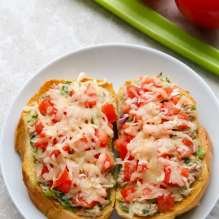 Overhead view of an Open-Faced Tuna Melt in a white plate with celery and tomatoes in the background.
