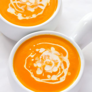 Overhead view of two bowls of Coconut Carrot Soup on a white background.