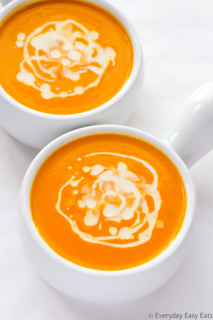 Overhead view of two bowls of Coconut Carrot Soup on a white background.