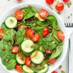 Overhead view of Cherry Tomato Spinach Salad in a white bowl against a light background.