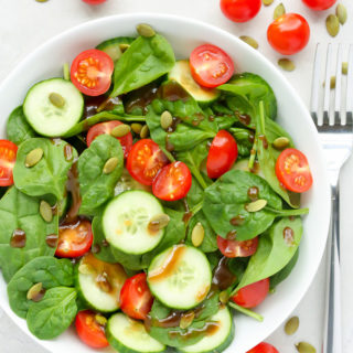 Overhead view of Tomato Spinach Salad in a white bowl against a light background.