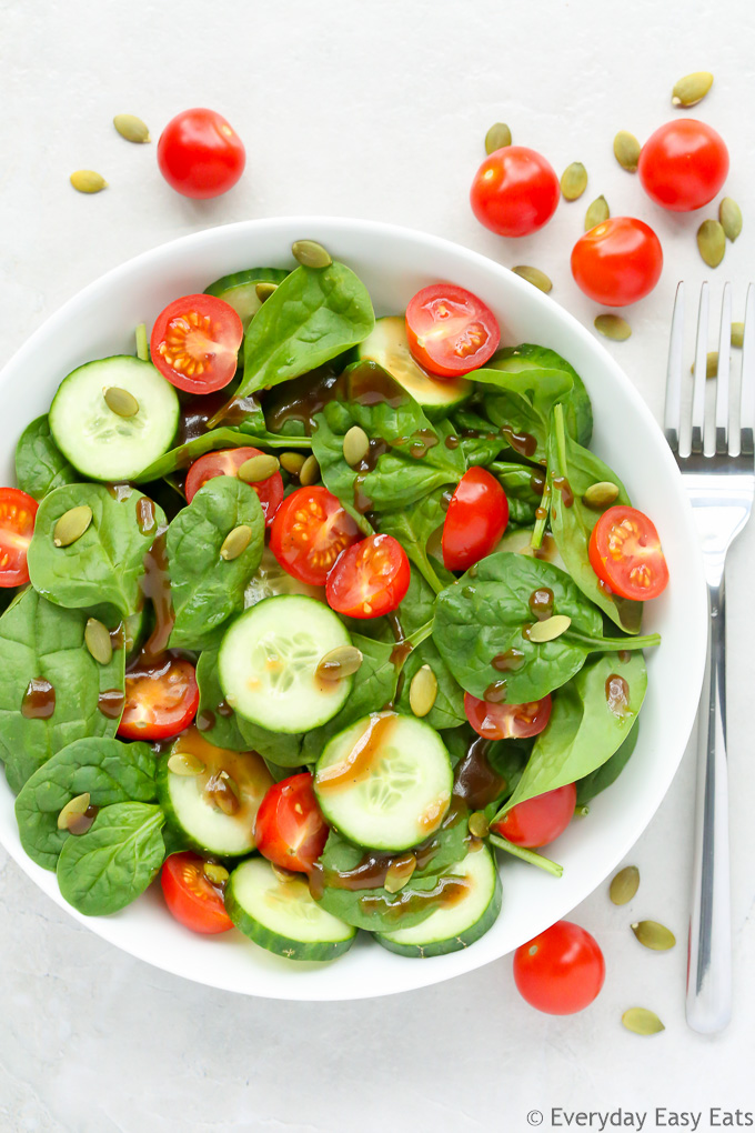 Overhead view of Tomato Spinach Salad in a white bowl against a light background.