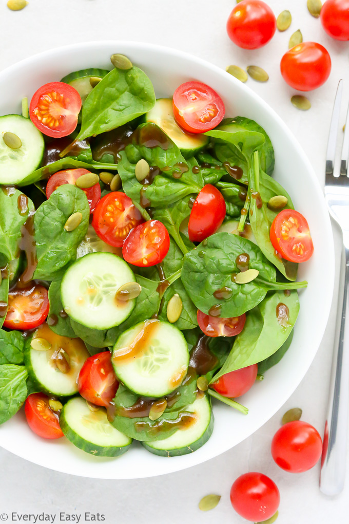 Close-up overhead view of Cherry Tomato Spinach Salad in a white bowl against a light background.