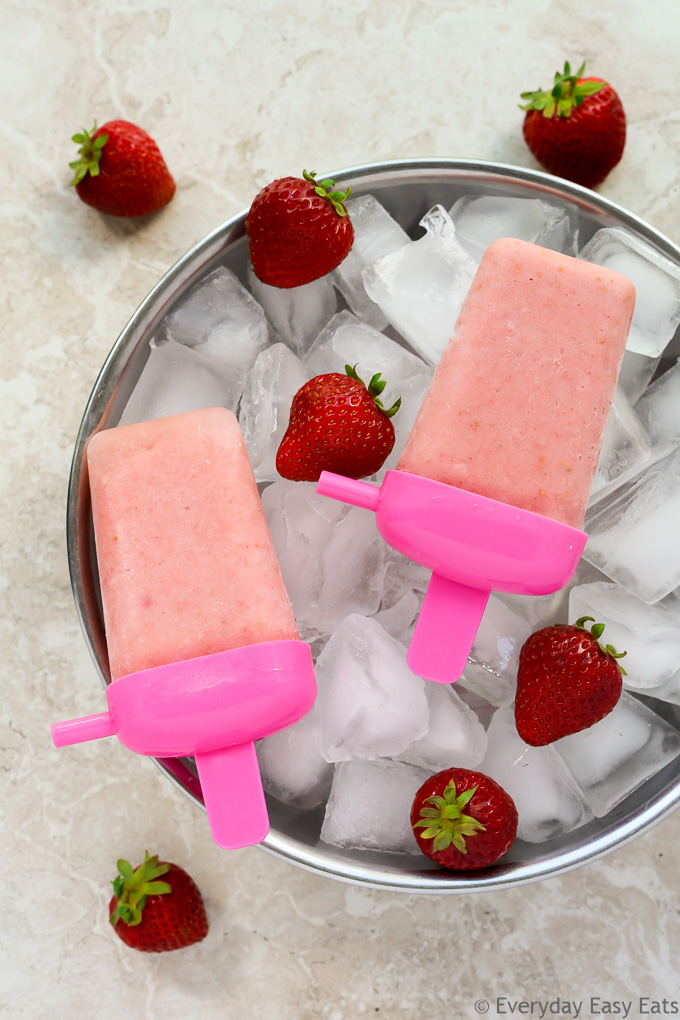 Overhead view of Creamy Strawberry Milk Popsicles on top of a large silver bowl filled with ice and fresh strawberries.