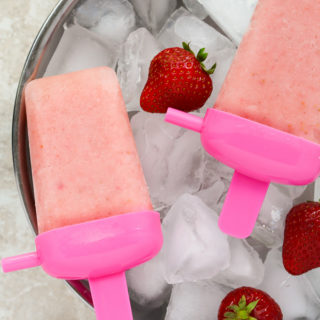 Close-up overhead view of Healthy Homemade Strawberry Popsicles on top of a large silver bowl filled with ice and fresh strawberries.