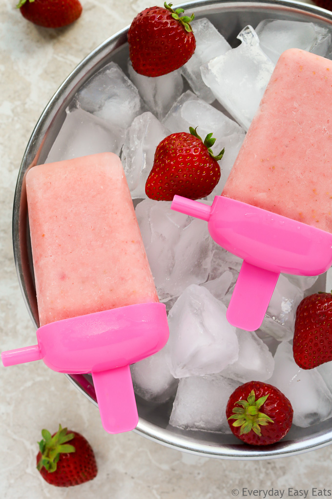 Overhead view of Creamy Strawberry Milk Popsicles resting on top of a large silver bowl filled with ice and fresh strawberries.