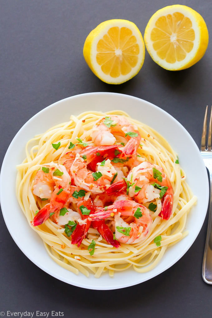 Overhead view of Garlic Shrimp Scampi in a white plate with lemon halves on the side against a black background.