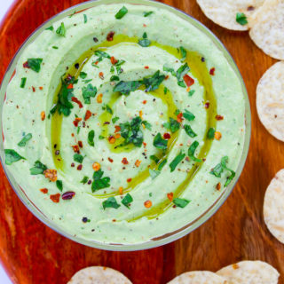 Close-up overhead view of a bowl of Healthy Avocado Dip on a wooden background with scattered tortilla chips.