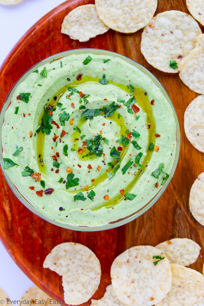 Close-up overhead view of a bowl of Yogurt Avocado Dip on a wooden background with scattered tortilla chips.