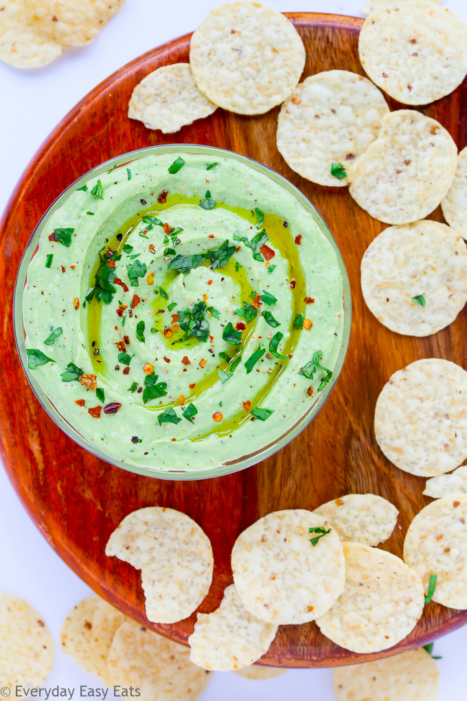 Close-up overhead view of a bowl of Healthy Avocado Dip on a wooden background with scattered tortilla chips.