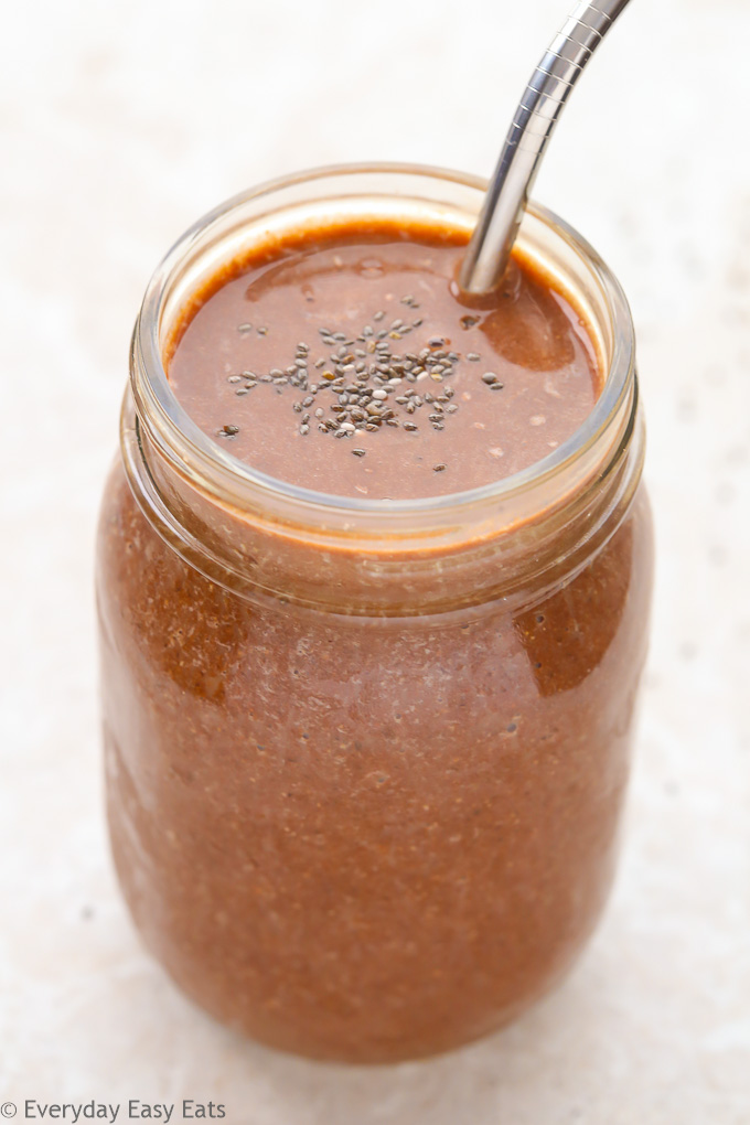 Side view of a mason jar full of Healthy Chocolate Milkshake with a straw against a light background.