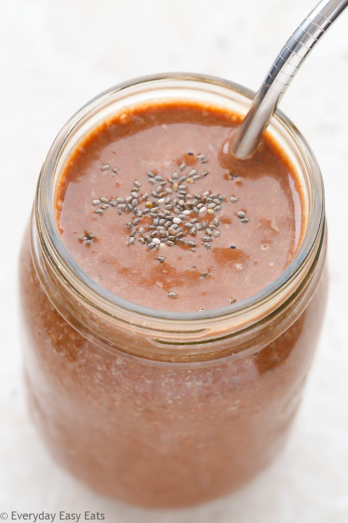 Close-up overhead view of a mason jar full of Healthy Chocolate Milkshake with a metal straw against a light background.