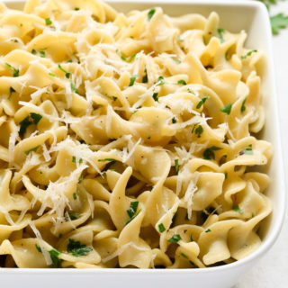 Close-up overhead view of Buttered Egg Noodles in a large white serving dish on a light surface.