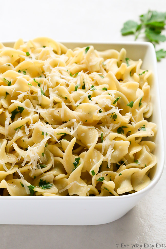 Close-up overhead view of Buttered Egg Noodles in a large white serving dish on a light surface.