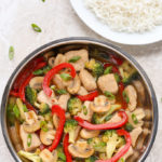 Overhead view of Chicken and Vegetable Stir-Fry in a wok with a plate of white rice beside it.