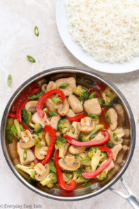 Overhead view of Healthy Chicken and Vegetable Stir-Fry in a wok with a plate of white rice beside it.