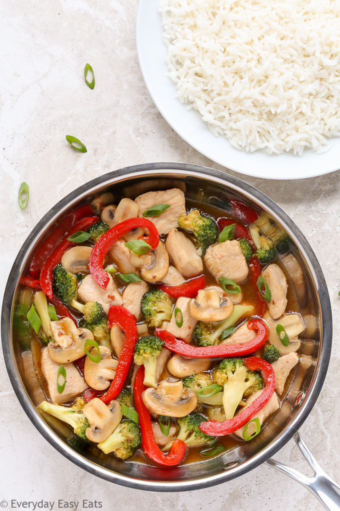 Overhead view of Chicken and Vegetable Stir-Fry in a wok with a plate of white rice beside it.