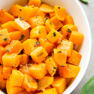 Close-up overhead view of a serving bowl of Roasted Butternut Squash with Sage on a grey background.