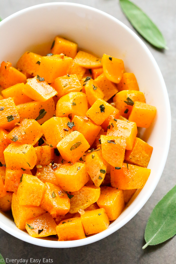 Close-up overhead view of a serving bowl of Roasted Butternut Squash with Sage on a grey background.