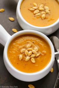 Close-up overhead view of two bowls of Butternut Squash Apple Soup with roasted butternut squash seeds sprinkled over top.