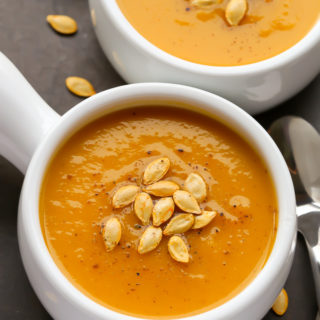 Close-up overhead view of two bowls of Butternut Squash Apple Soup with roasted butternut squash seeds sprinkled over top.