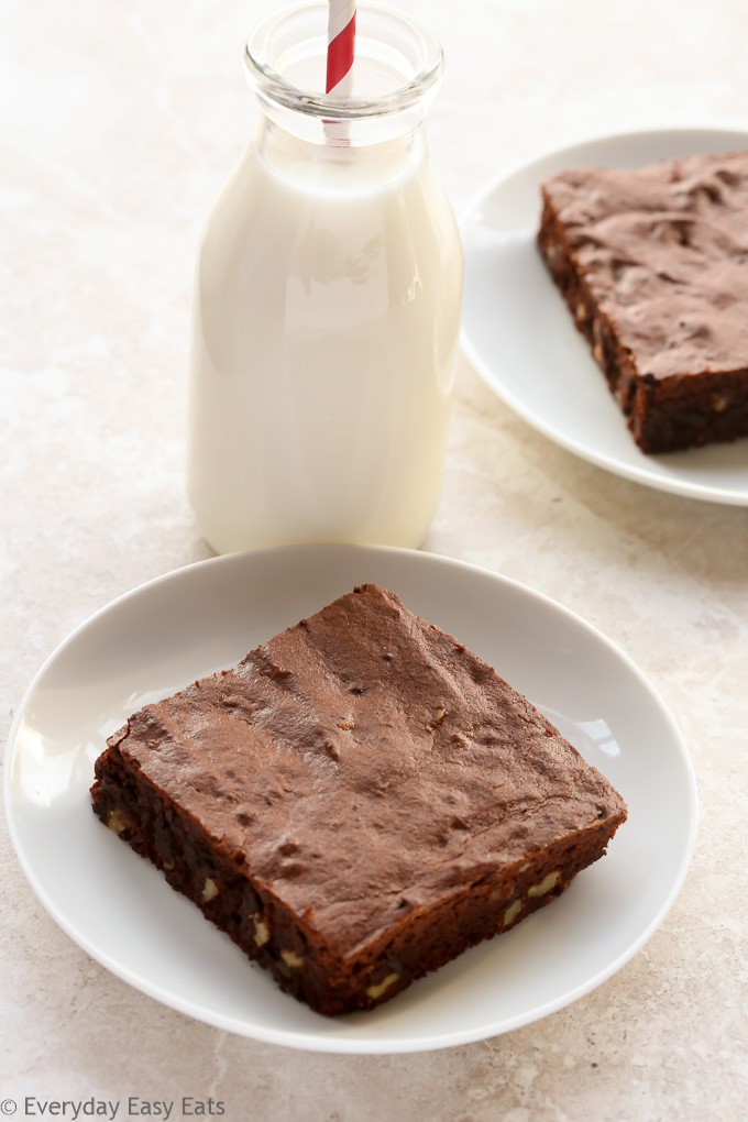 Overhead view of Fudgy Cocoa Brownies in white plates with a glass of milk on a neutral background.