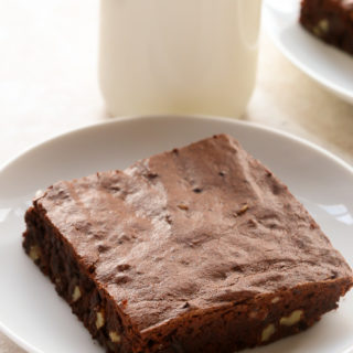 Overhead view of Fudgy Cocoa Brownies in white plates with a glass of milk on a neutral background.