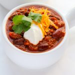 Overhead view of Ground Beef Chili in a white bowl on a white background with title text overlay.