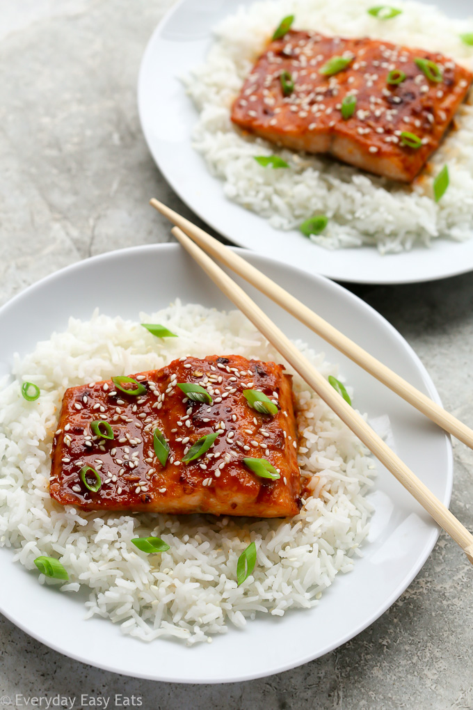 Overhead view of two plates of Baked Honey Sriracha Salmon sitting on a bed of white rice with chopsticks.