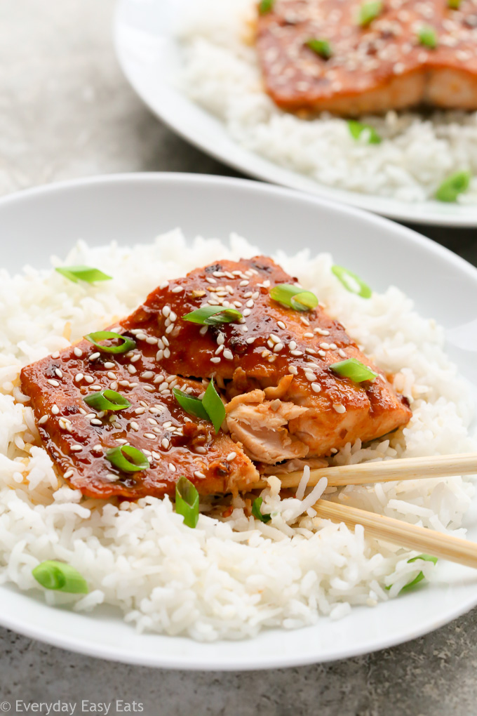 Close-up view of a plate of Baked Honey Sriracha Salmon on a bed of white rice with chopsticks.