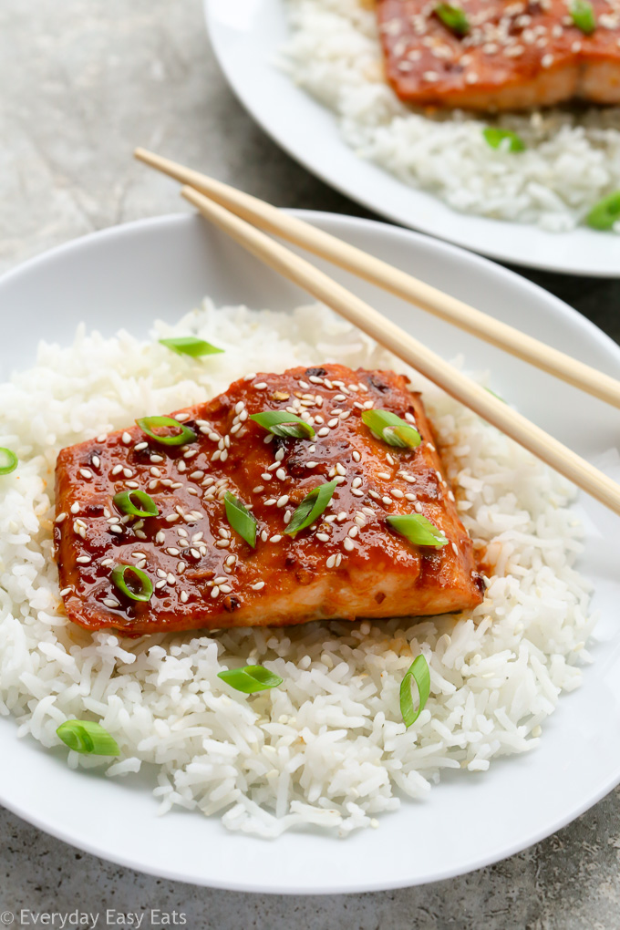 A plate of Baked Honey Sriracha Salmon sitting on a bed of white rice with chopsticks.