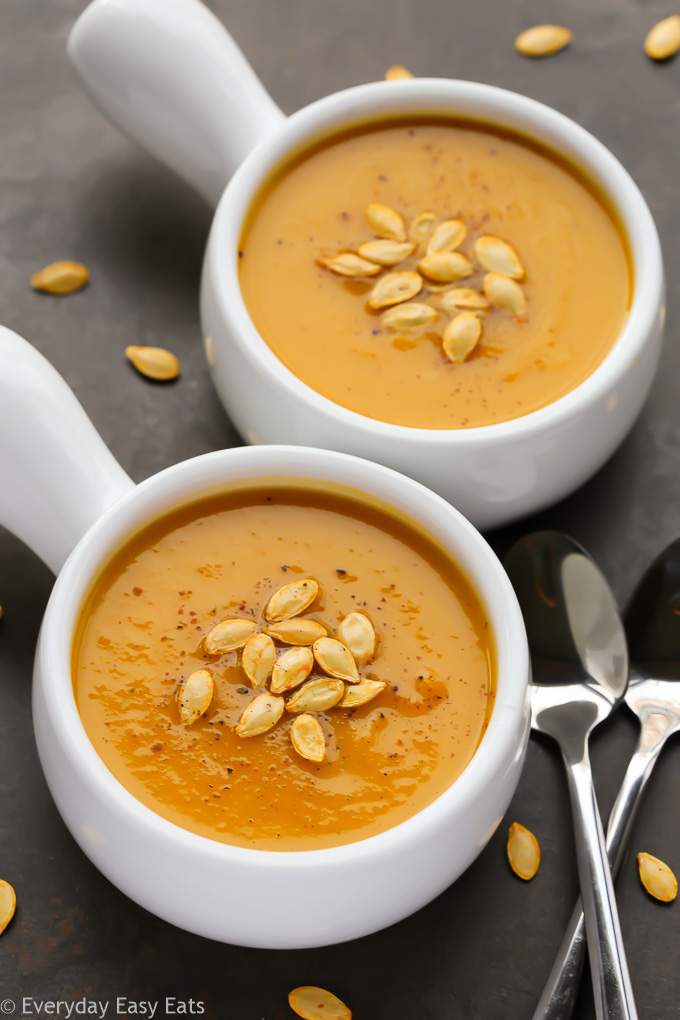 Overhead view of two bowls of Butternut Squash Apple Soup with roasted butternut squash seeds sprinkled over top.