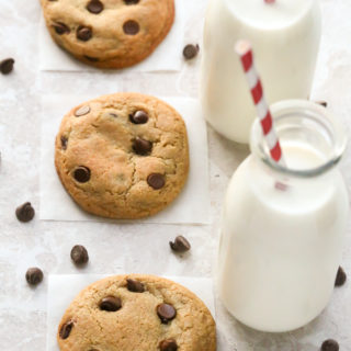 Overhead view of No-Chill Chocolate Chip Cookies with Cornstarch with glasses of milk and scattered chocolate chips on a neutral background.