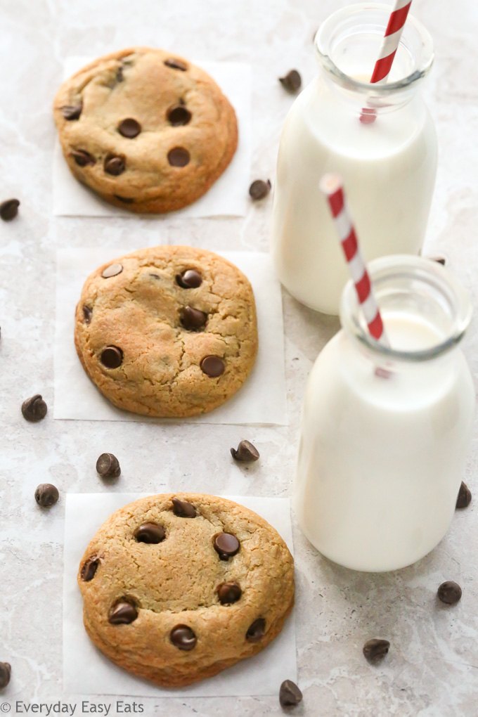 Overhead view of The Best Soft and Chewy Chocolate Chip Cookies with glasses of milk and scattered chocolate chips on a neutral background.