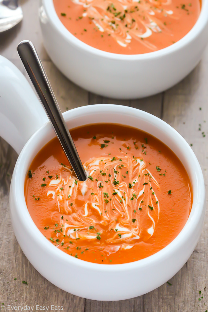 Close-up overhead view of two bowls of Cream of Tomato Soup against a wooden background.