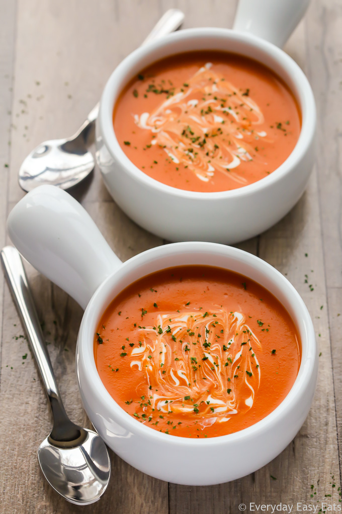 Overhead view of two bowls of Creamy Tomato Soup against a wooden background.