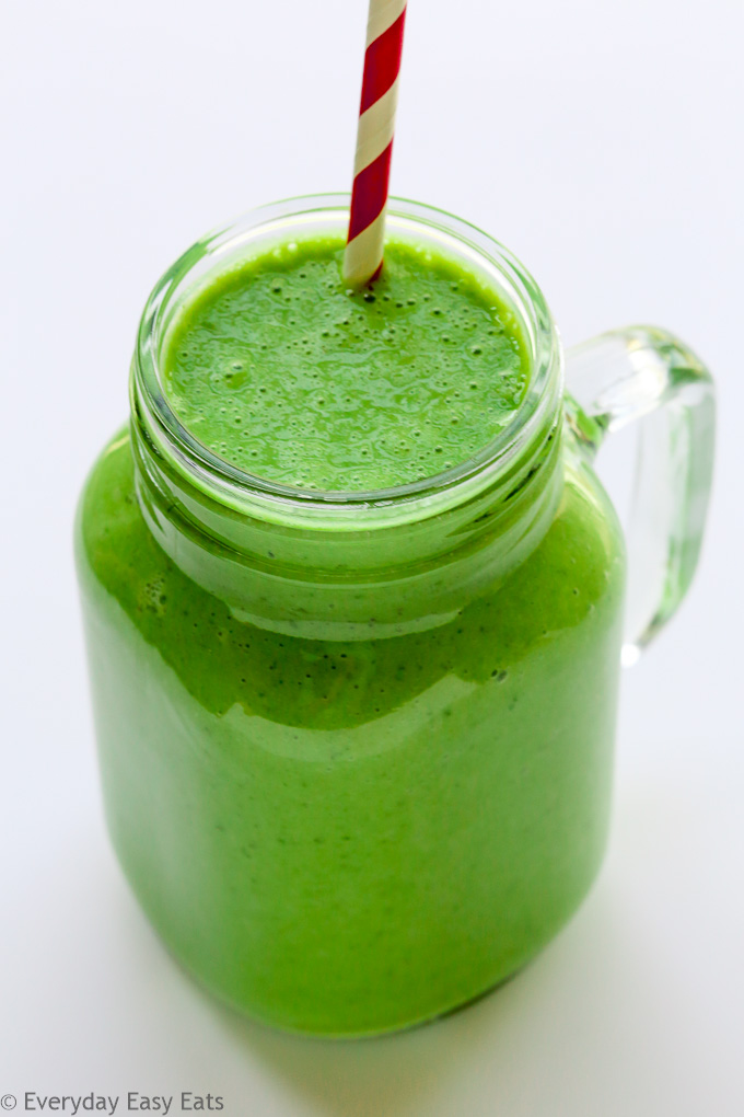 Overhead view of a mason jar full of a Green Smoothie with a straw against a light background.