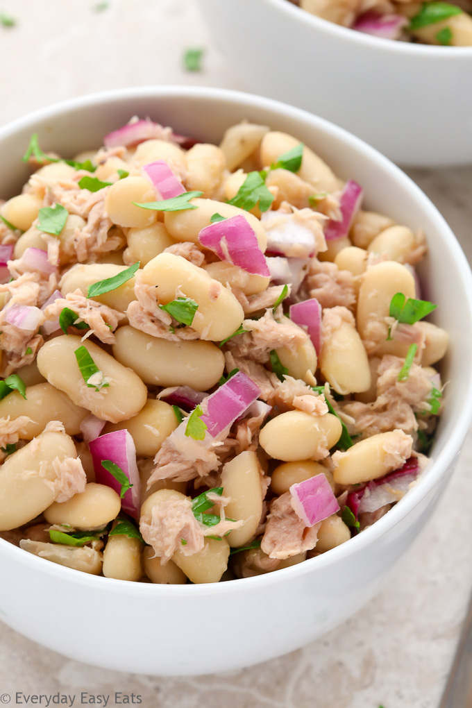 Close-up overhead view of a bowl of Tuna White Bean Salad on a neutral-colored background.