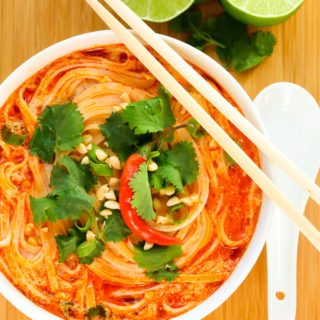 Overhead view of Thai Spicy Noodle Soup in a white bowl with chopsticks on a wooden background.