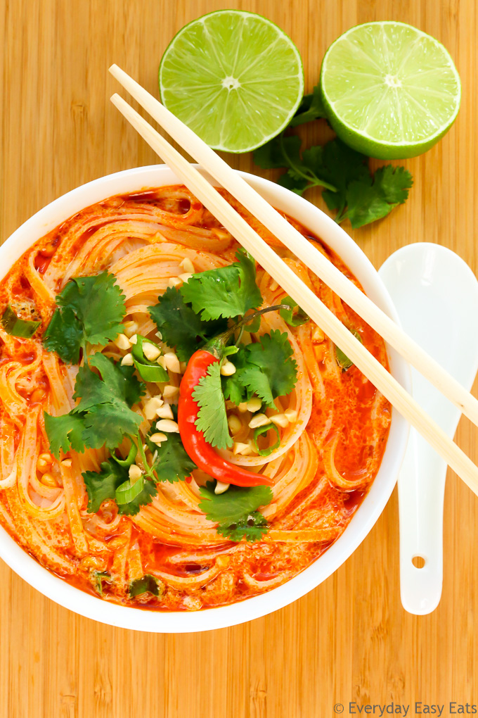 Overhead view of Thai Spicy Noodle Soup in a white bowl with chopsticks on a wooden background.