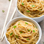Overhead view of two bowls of Chinese Sesame Noodles with chopsticks on the side on a neutral background.