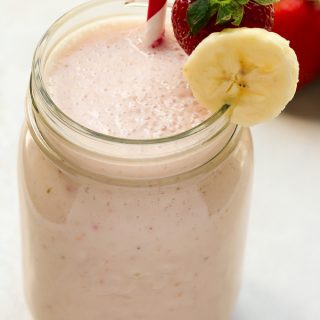 Close-up overhead view of a mason jar full of Strawberry Banana Smoothie with a straw against a light background.