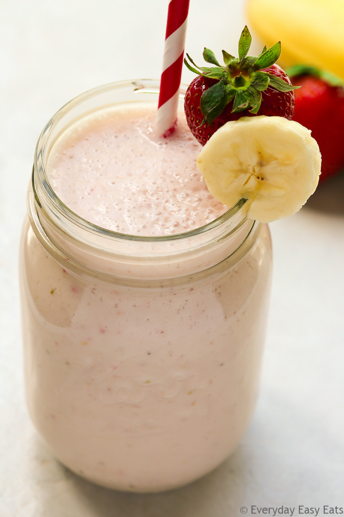 Close-up overhead view of a mason jar full of Strawberry Banana Smoothie with a straw against a light background.