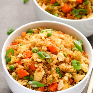 Overhead view of two bowls of Vegetarian Quinoa Fried Rice on a dark background with chopsticks on the side.