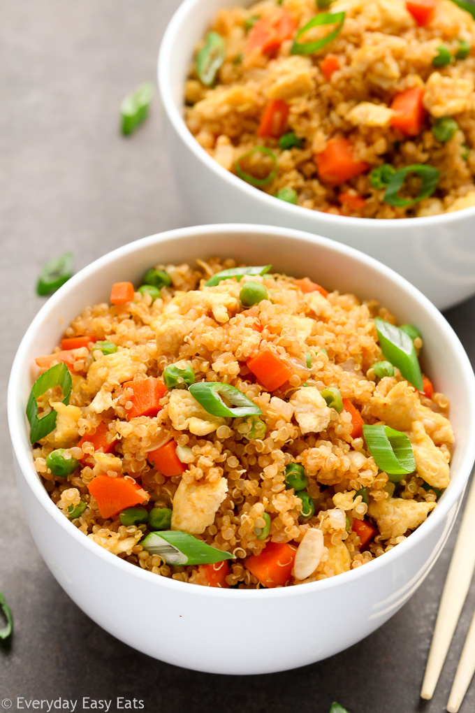 Overhead view of two bowls of Vegetarian Quinoa Fried Rice on a dark background with chopsticks on the side.