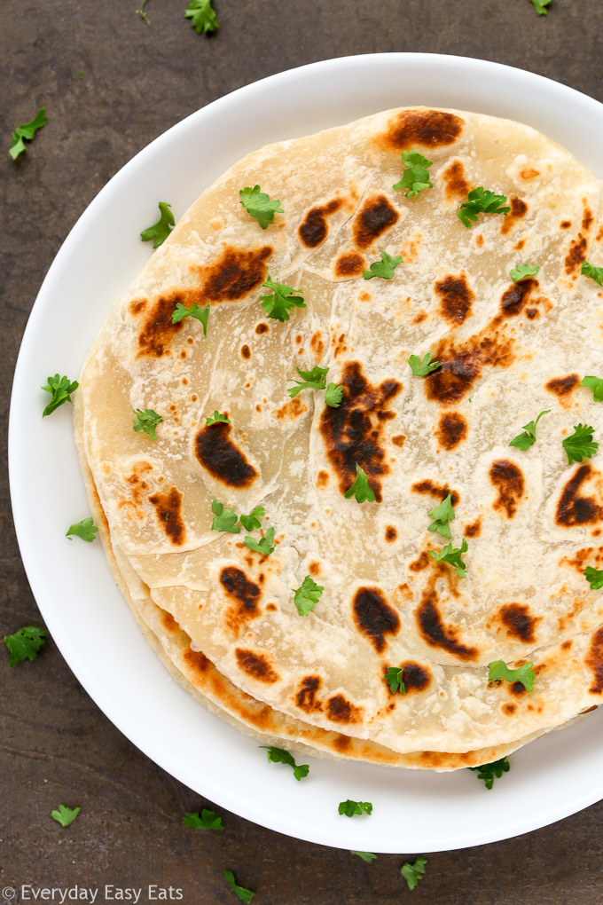 Overhead view of a stack of Easy Homemade No-Yeast Flatbread in a white plate on a dark background.