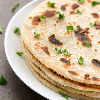 Side view of a stack of Easy Homemade No-Yeast Flatbread in a white plate on a dark background.