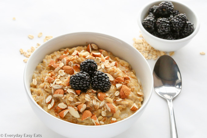 Overhead view of Brown Sugar Oatmeal in a white bowl and spoon on the side, topped with chopped almonds and blackberries.