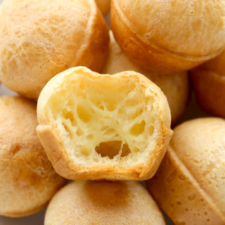 Side view of Brazilian Cheese Bread (Pão de Queijo) in a white plate, one piece has a bite taken out of it.